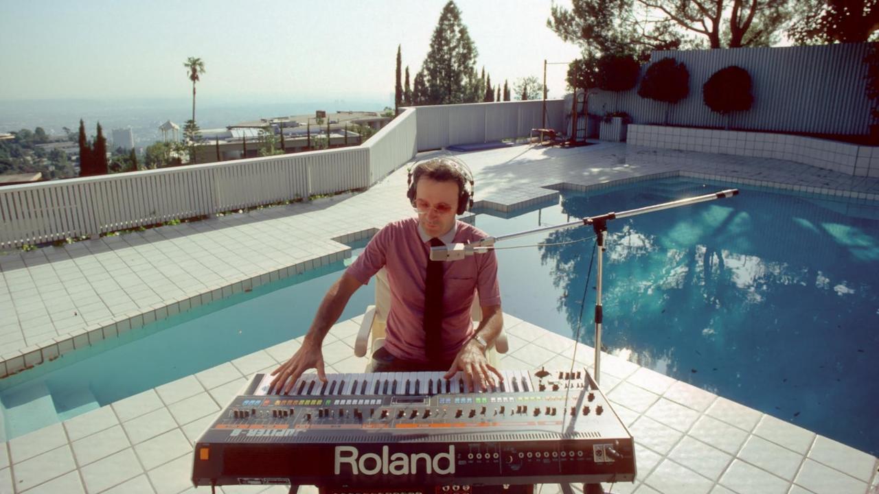 Giorgio Moroder sitzt an einem Pool und spielt auf einem Keyboard. 
