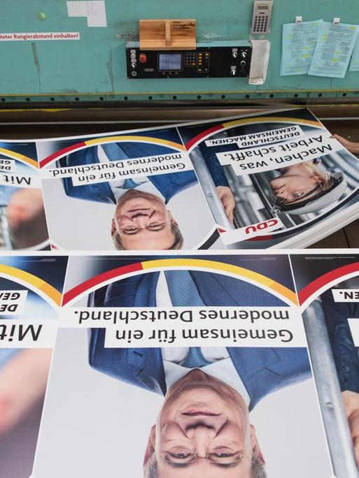 Druckereimitarbeiter legen Wahlplakate der CDU mit einem Bild des Parteivorsitzenden und Bundeskanzlerkandidaten Armin Laschet darauf in eine Zuschneidemaschine.