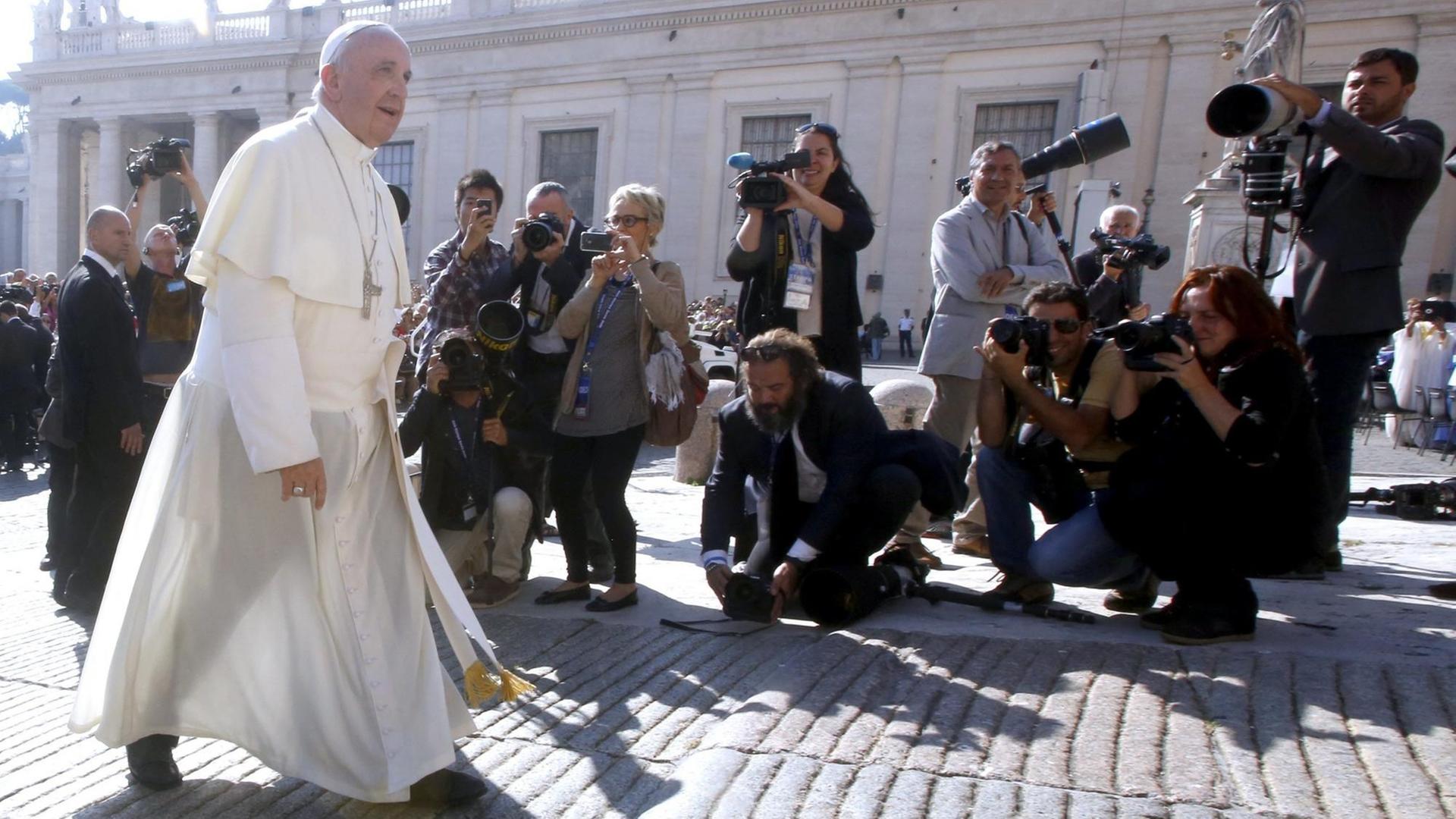 Papst Franziskus läuft an Journalisten mit Kameras vorbei.