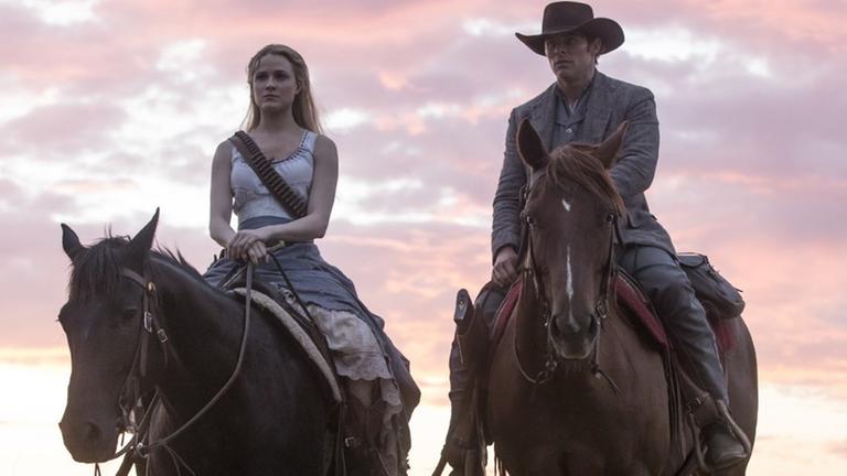 Evan Rachel Wood und James Marsden reiten auf Pferden vor dem Hintergrund eines Sonnenuntergangs.