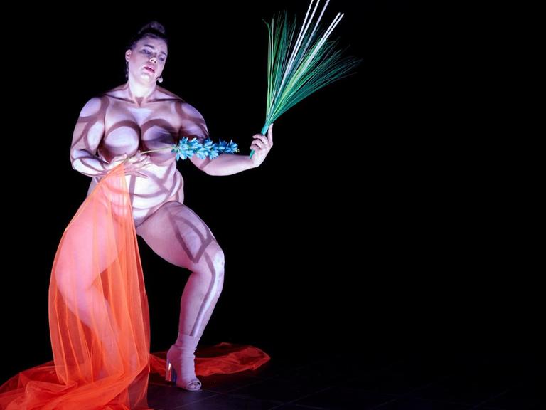 Eine mollige Frau tanzt nackt und bemalt.