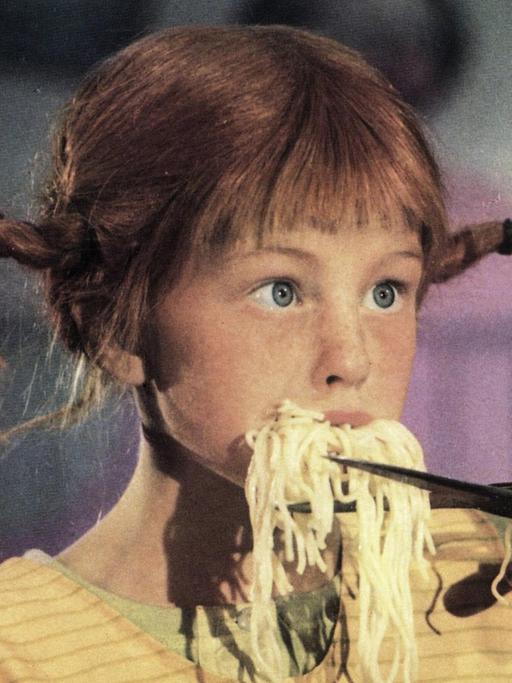 Pippi Langstrumpf hat den Mund voll Spaghetti und schneidet sie mit einer Schere ab.