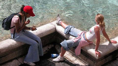 Zwei Touristinnen sitzen am Trevibrunnen in Rom.