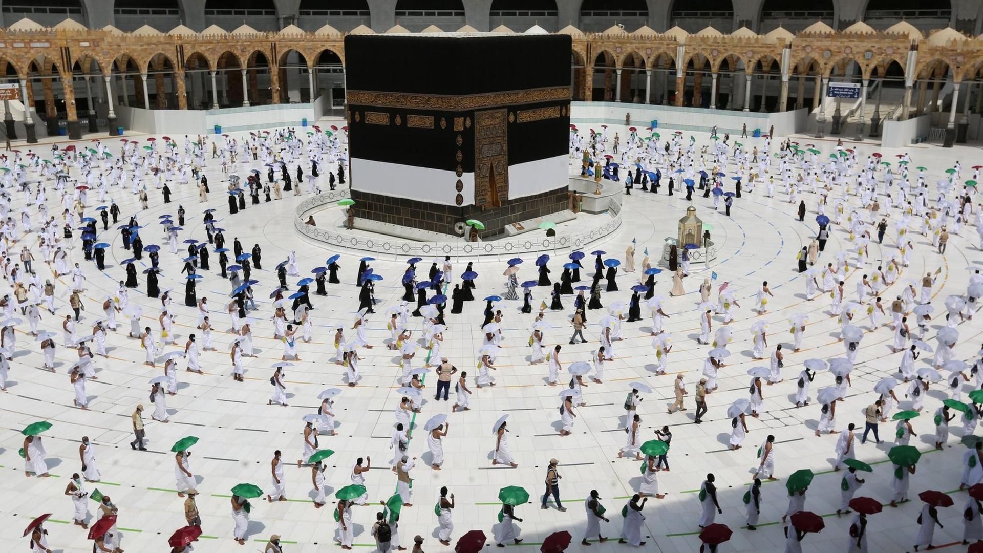 Menschen gehen mit großem Abstand zueinander um die Kaaba in der Großen Moschee von Mekka herum. Menschen gehen mit großem Abstand zueinander um die Kaaba in der Großen Moschee von Mekka herum.