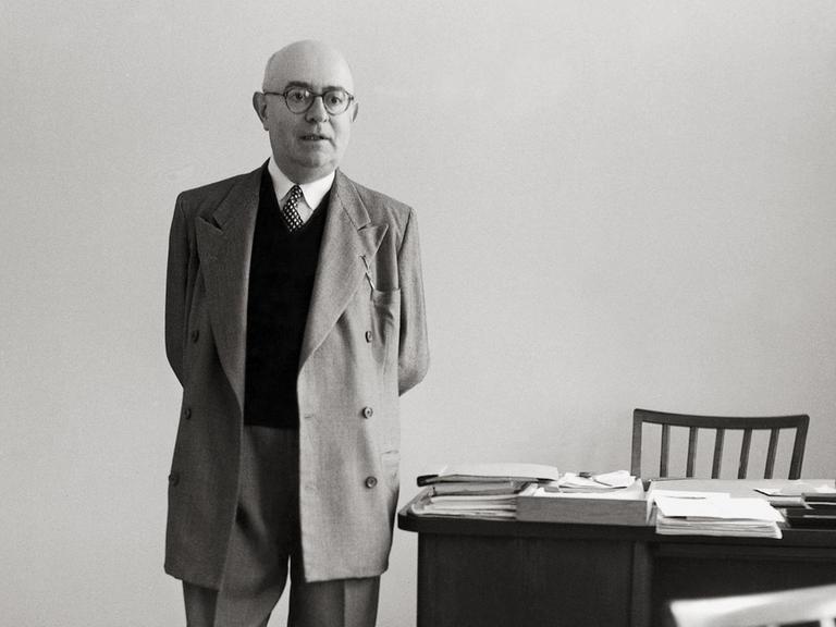 Die Aufnahme von 1958 zeigt den Philosophen Theodor W. Adorno mit hinter dem Rücken verschränkten Händen neben seinem Schreibtisch stehend.