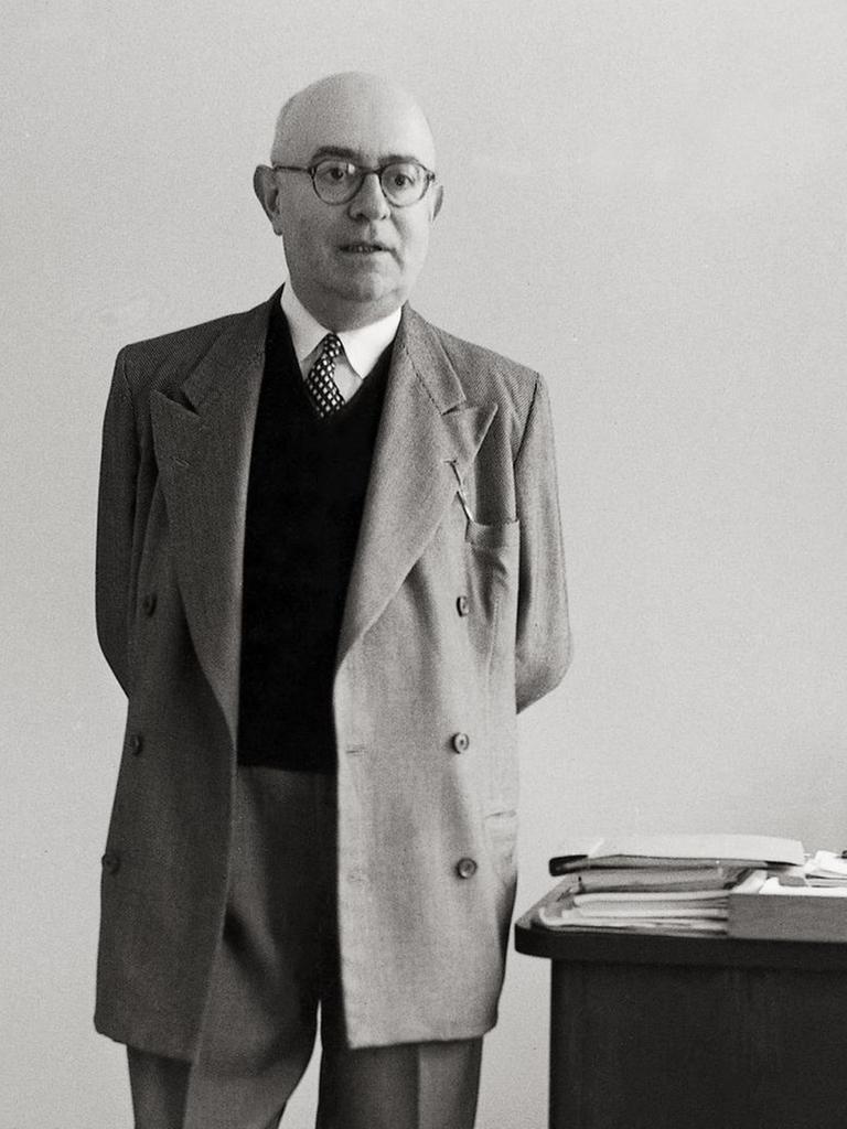 Die Aufnahme von 1958 zeigt den Philosophen Theodor W. Adorno mit hinter dem Rücken verschränkten Händen neben seinem Schreibtisch stehend.