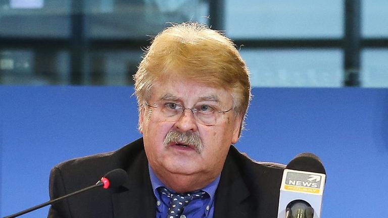 Elmar Brok sitzt an einem Tisch und spricht in ein Mikrofon