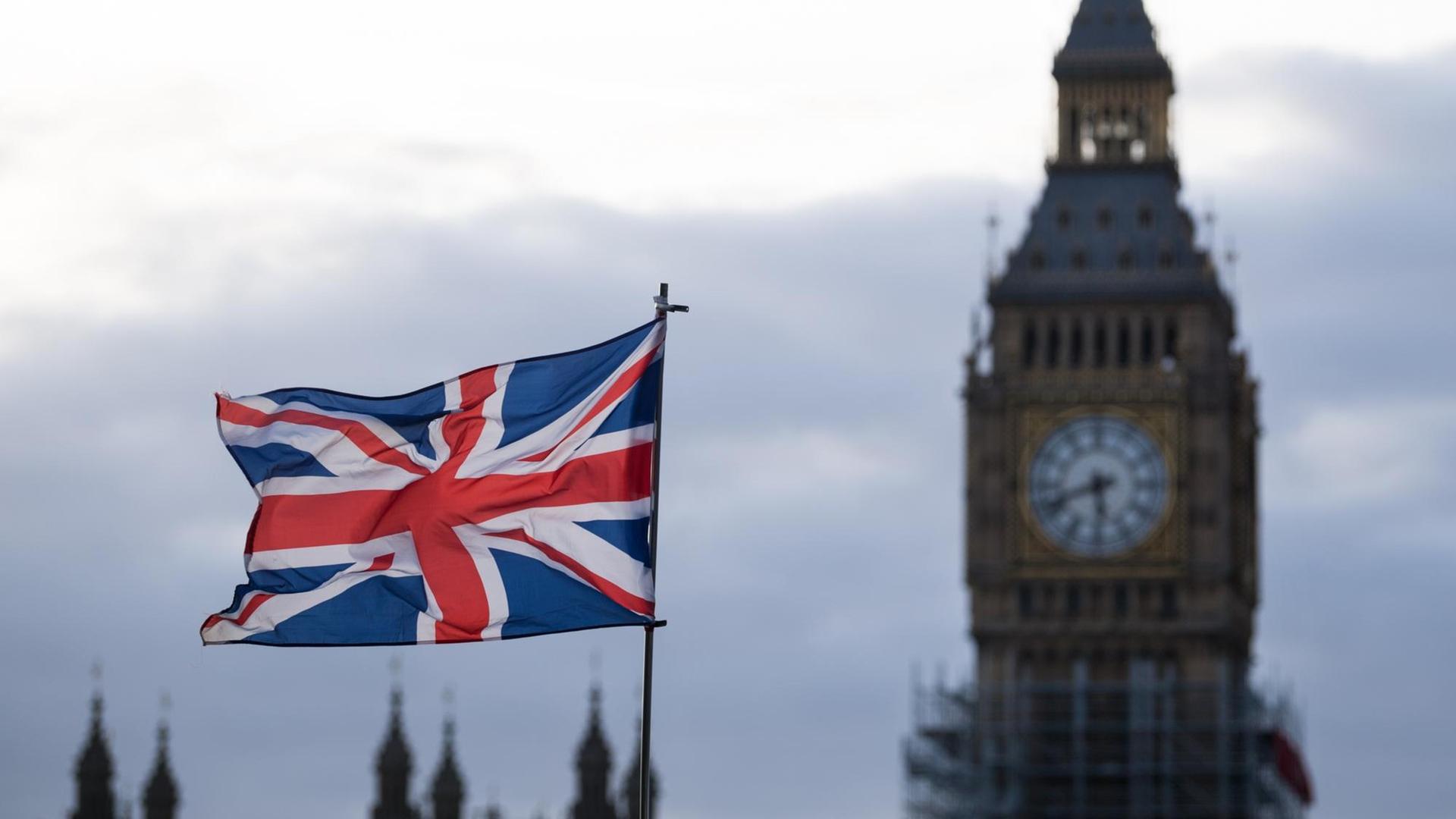 Eine Fahne vom Vereinigtem Königreich (Union Jack) weht in London im Wind. Im Hintergrund ist der Uhrturm Elizabeth Tower mit dem Big Ben zu sehen.
