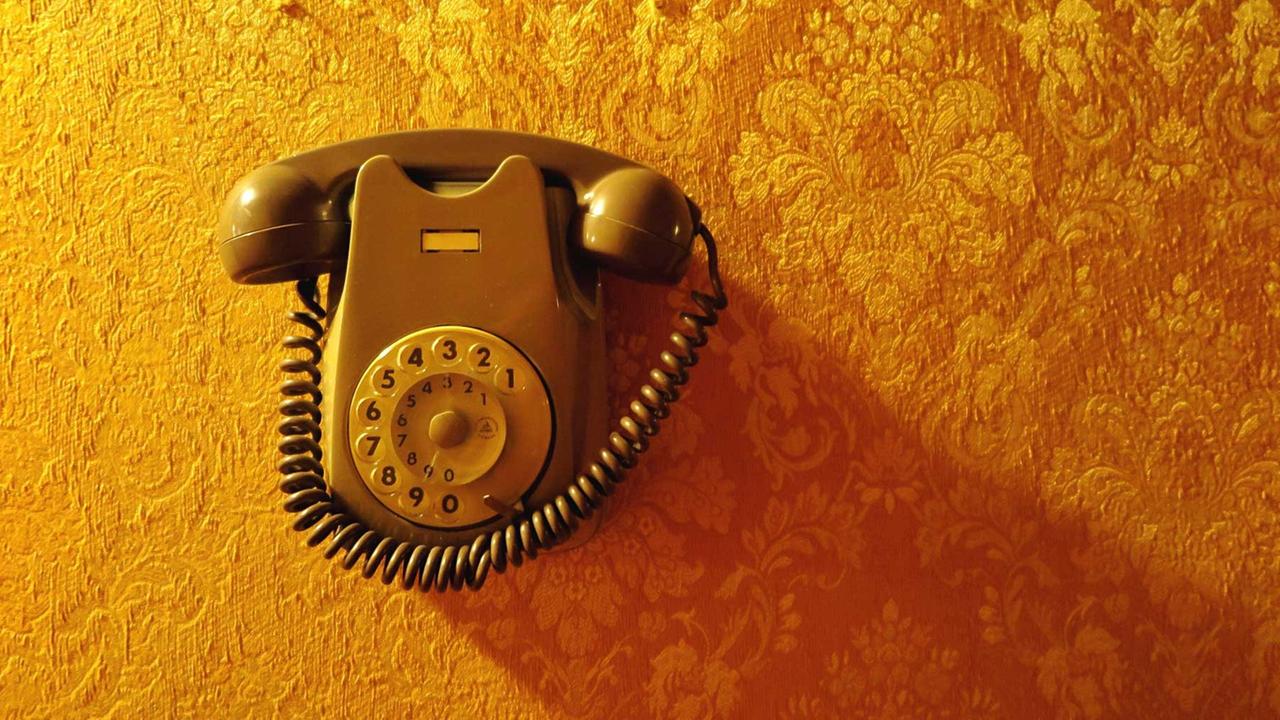 Ein altes Telefon mit Wahlscheibe vor einer Vintage-Tapete.