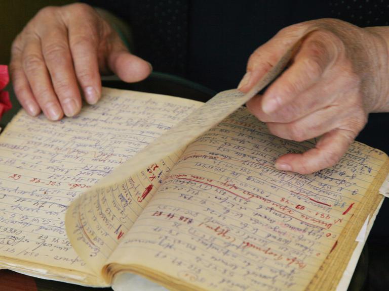 Eine ältere Frau blättert in einem Notizbuch - ihre Hände sind zu sehen.