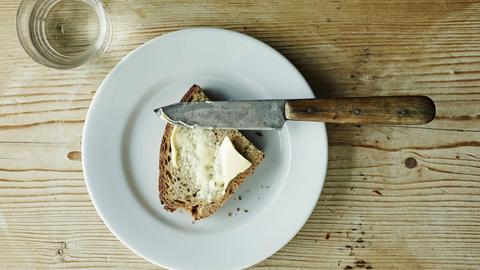 Auf einem Tisch stehen ein Wasserglas und eine Scheibe Brot mit Butter.