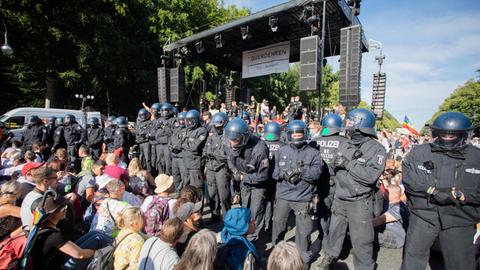 Polizisten stehen bei einer Kundgebung gegen die Corona-Beschränkungen auf der Straße des 17. Juni zwischen Teilnehmern vor einer Bühne.