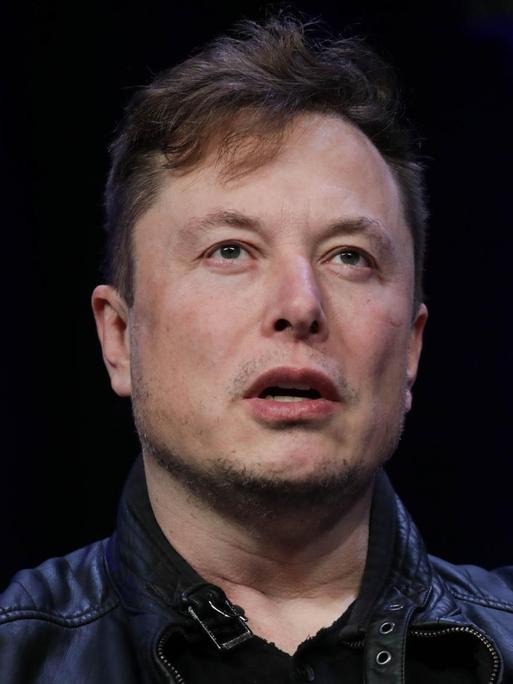 Oberkörperporträt von Elon Musk. Er trägt ein schwarze Jacke und darunter ein ebenfalls schwarzes Oberteil.