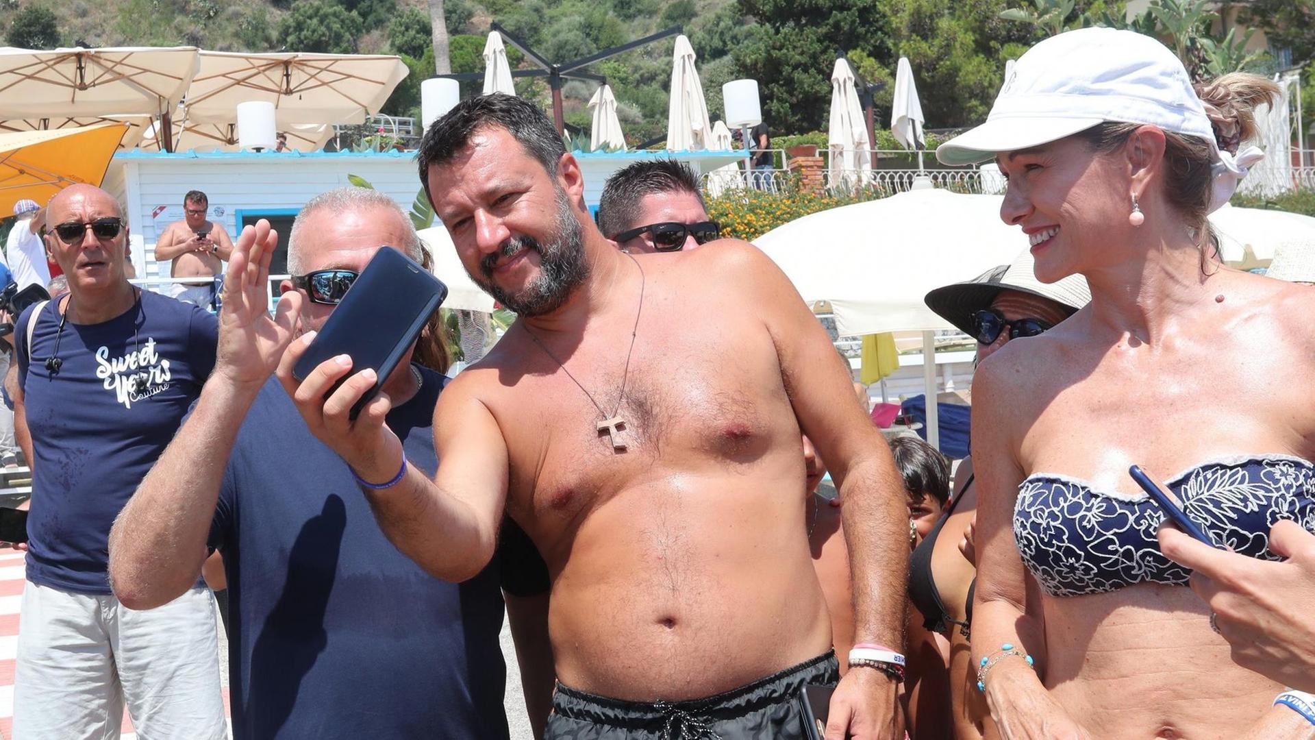 Das Foto zeigt Italiens Innenminister Matteo Salvini, der am Strand zusammen mit einem Mann ein Selfie macht.