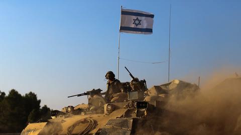 Israelische Soldaten mit Maschinengewehren fahren in einem Panzer, der reichlich Staub aufwirbelt, auf ihm steckt eine israelische Flagge
