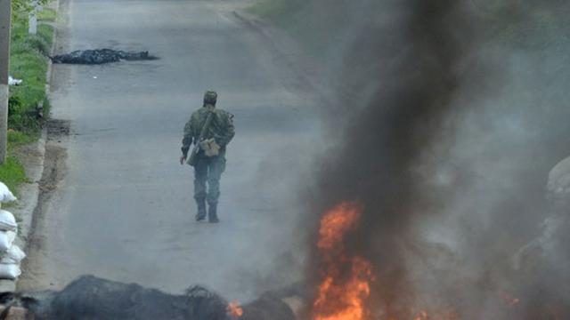 Ein bewaffneter, uniformierter pro-russischer Kämpfer läuft an einer brennenden Straßensperre an einem Checkpoint in der ukrainischen Stadt Slawjansk vorbei.