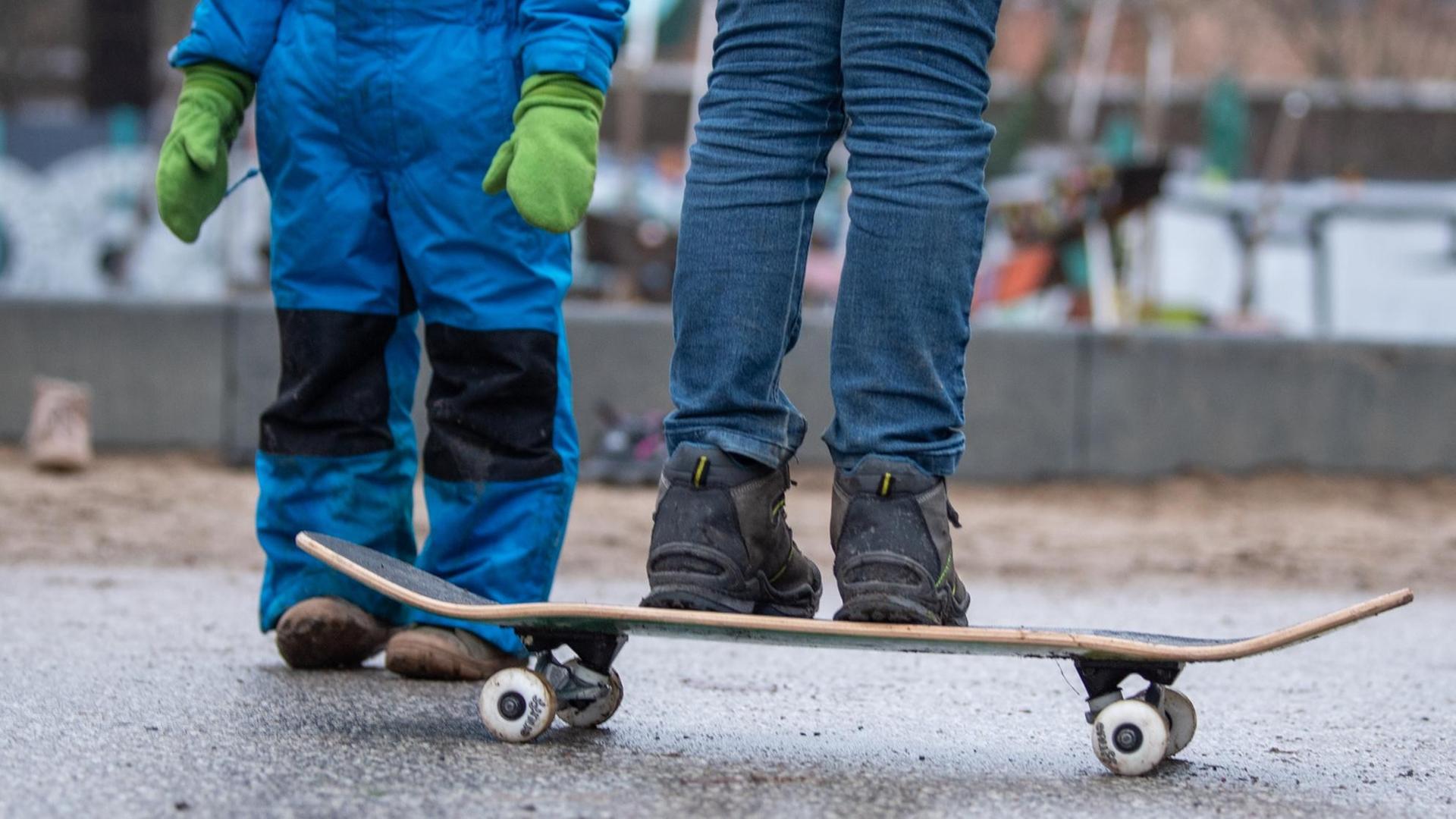 Zwei Kinder stehen bei einem Spielplatz in Berlin. Ein Kind balanciert auf einem Skateboard.