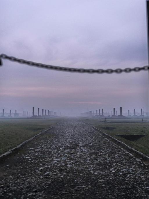 Sonnenaufgang im Morgennebel vor den halb offenen Drahttoren des Vernichtungslagers Auschwitz-Birkenau in Oswiecim, Polen.