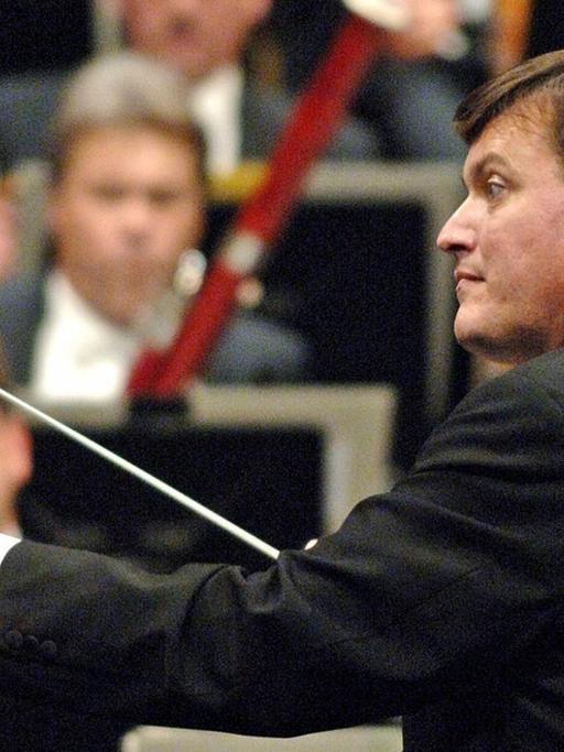 Der Dirigent steht vor einem Orchester und hebt seinen Dirigentenstab.