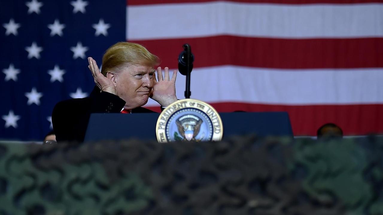US-Präsident Donald Trump auf Kurzbesuch bei den US-Soldaten in Afghanistan. Er steht an einem Redepult und hält sich die Hände an die Ohren, als warte er auf eine Reaktion des Publikums.