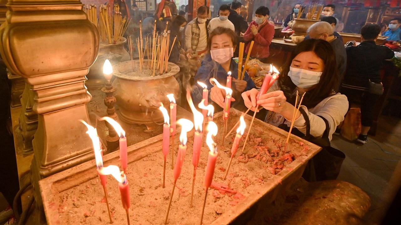 Frauen mit Mundschutz zünden in einem Tempel Räucherstäbchen und Kerzen an