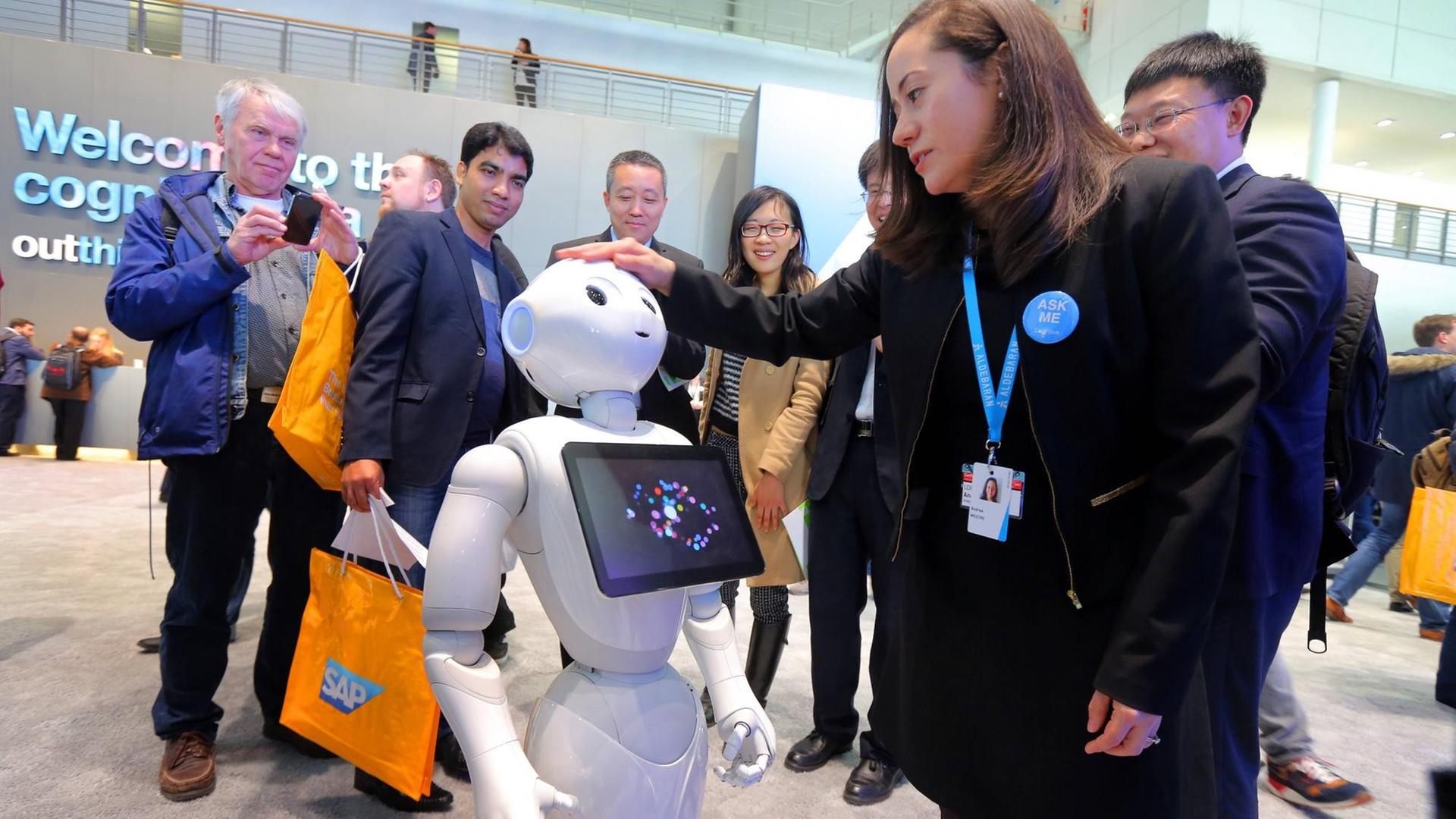 Man sieht den weißen Roboter Pepper. Eine Frau streichelt ihm über den Kopf.
