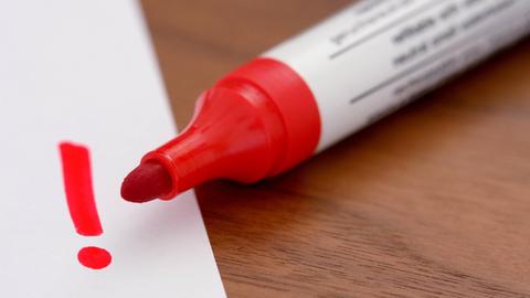 Ein roter Filzstift malt ein Ausrufezeichen auf ein Blatt Papier.