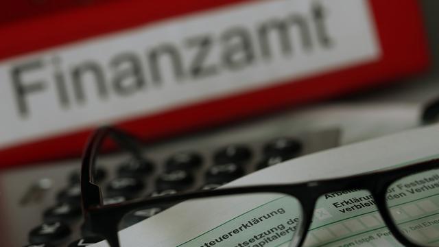 Ein Formular für die Einkommen-Steuer-Erklärung liegt vor einem Akten-Ordner mit der Aufschrift "Finanz-Amt".