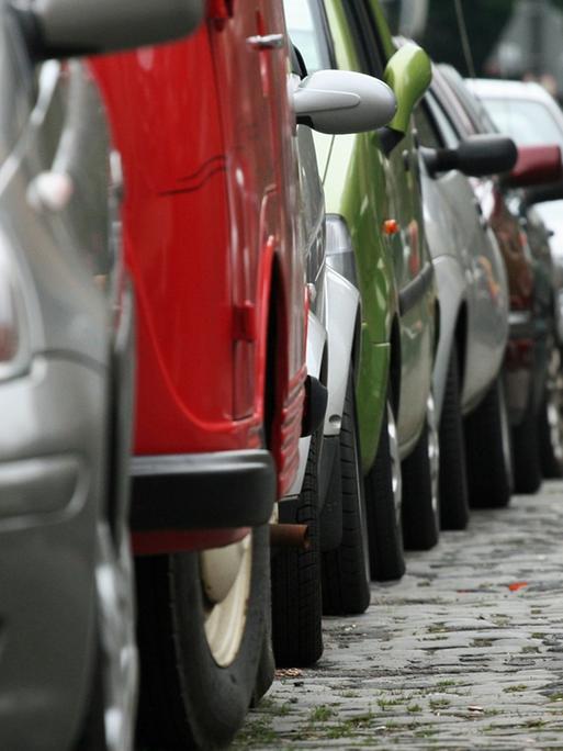 Auf einer Straße mit Kopfsteinpflaster in Köln parkt eine lange Reihe von Autos.