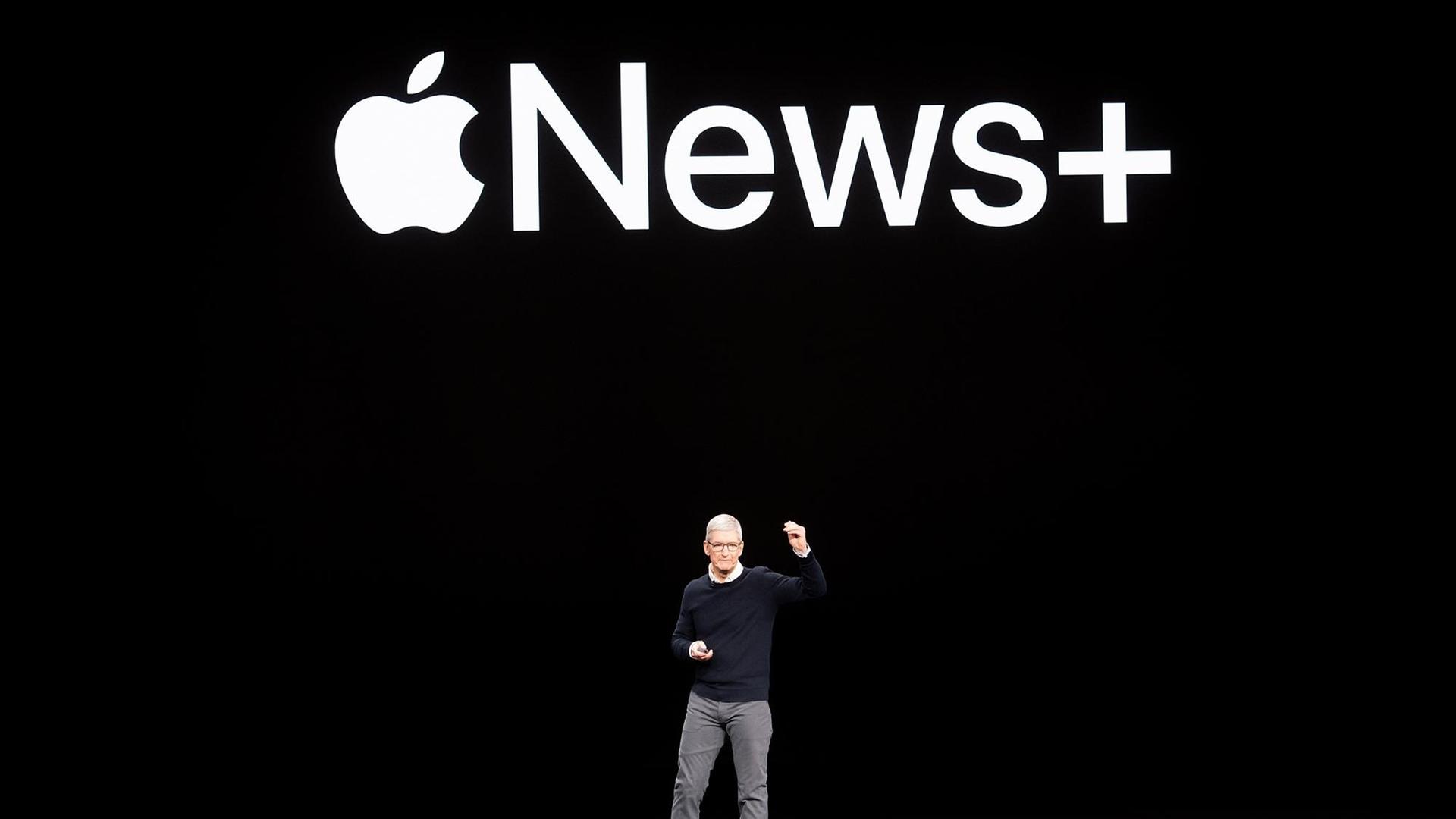 Der Chef des Technologieunternehmens Apple, Tim Cook, steht auf der Bühne. Auf der schwarzen Wand hinter ihm ist das Logo von Apple News Plus zu sehen.