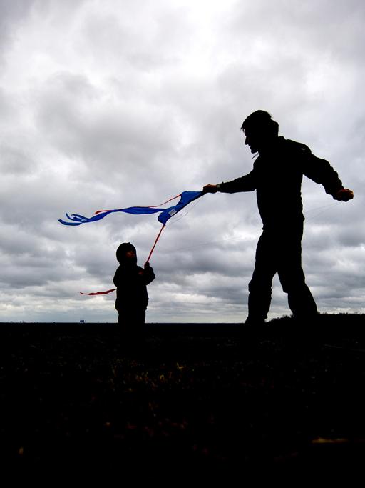 Ein Vater lässt am 16.03.2014 in Berlin auf dem Teufelsberg bei starkem Wind und dicht bewölktem Himmel mit seinem Sohn einen Drachen steigen.