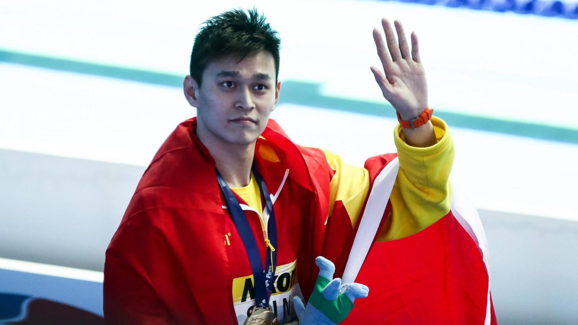 Sun Yang trägt die chinesische Flagge um den Oberkörper und winkt mit der linken Hand.