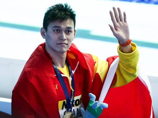 Sun Yang trägt die chinesische Flagge um den Oberkörper und winkt mit der linken Hand.
