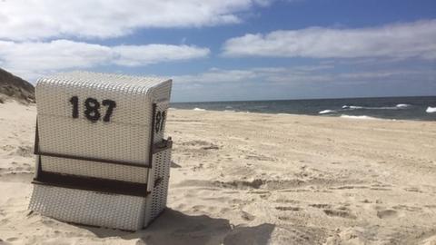 Ein weißer Strandkorb mit der Nummer 187 steht mit der Rückseite zum Betrachter an einem menschenleeren Strand.