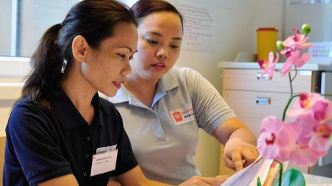 Pflegerin Janette Dela Cruz (l.) von den Philippinen wird im Caritas Altenheim St. Nikolaus in München von einer Kollegin eingewiesen.