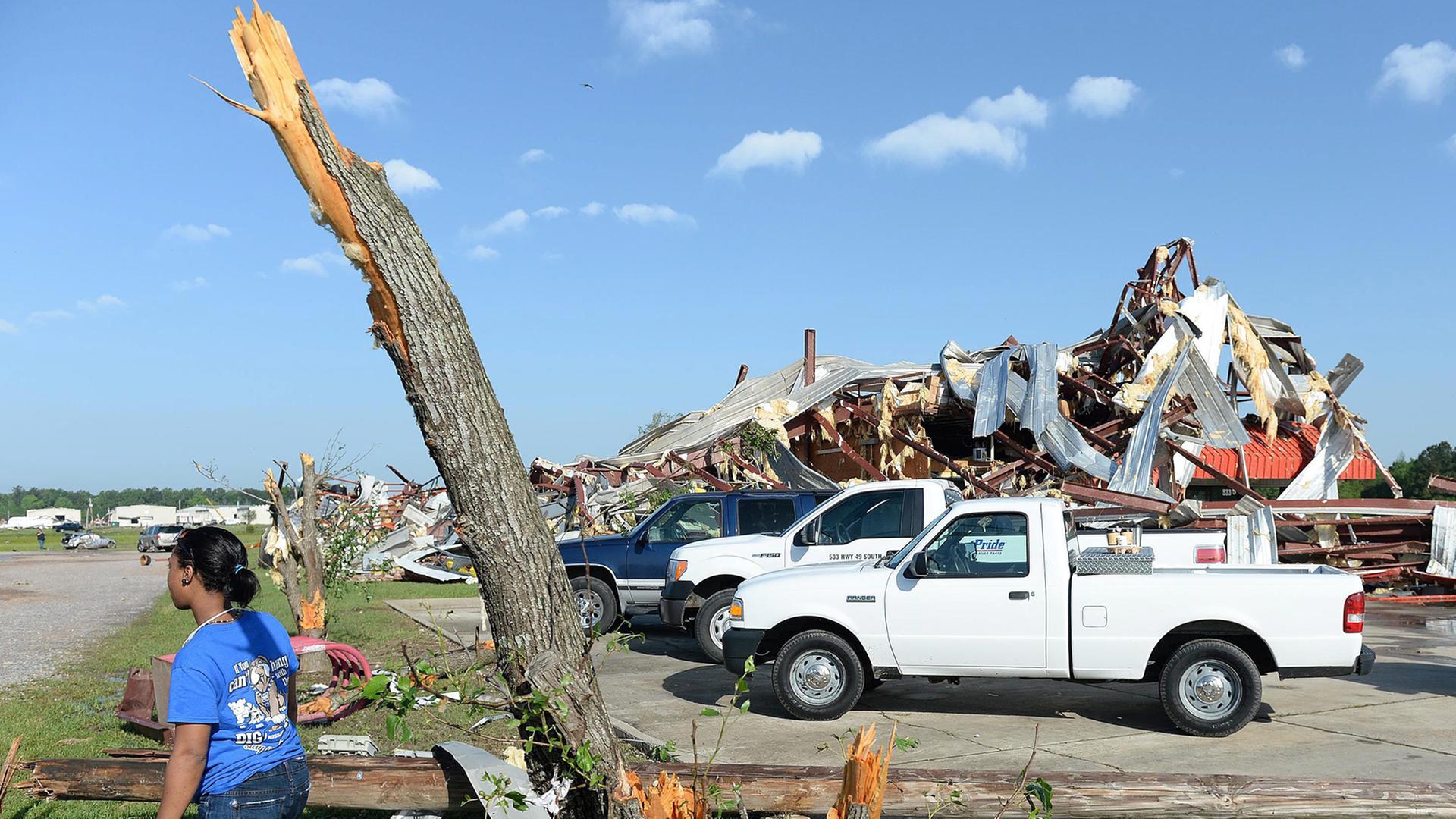 Eine Frau steht neben einem Baumstumpf, dahinter stehende Gebäude sind total zerstört.