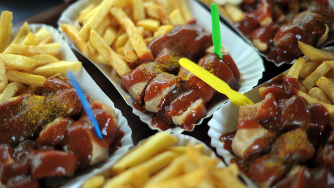Mehrere Pappteller mit Currywurst und Pommes Frites stehen auf einem Tisch. 