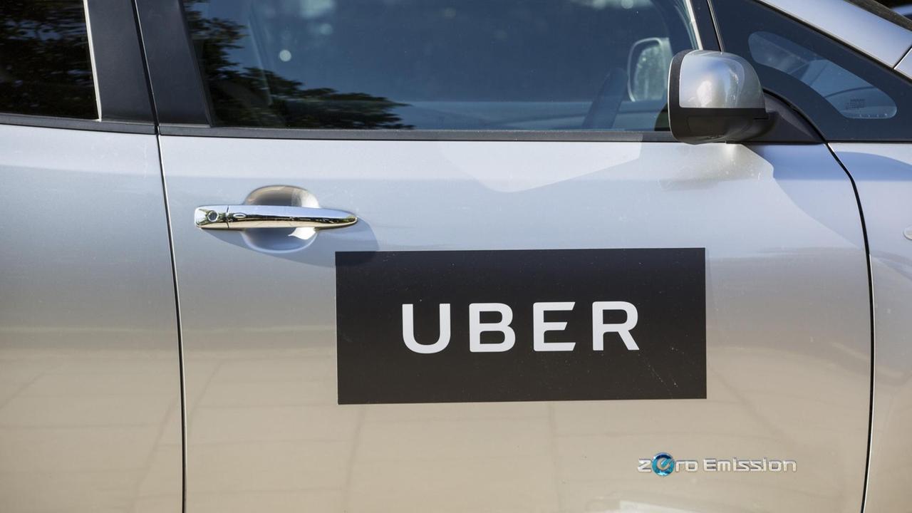 Das Logo des Fahrzeug-Vermittlungsdienstes Uber auf der Seitentüre eines grauen Pkw.