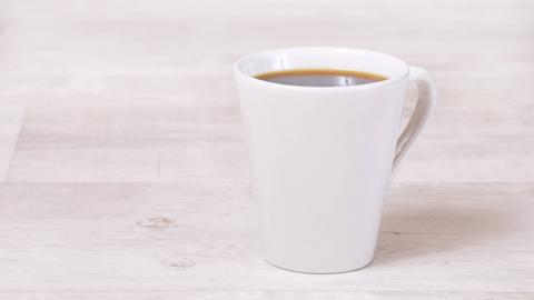 Eine volle Kaffeetasse steht auf einem hellen Holztisch.