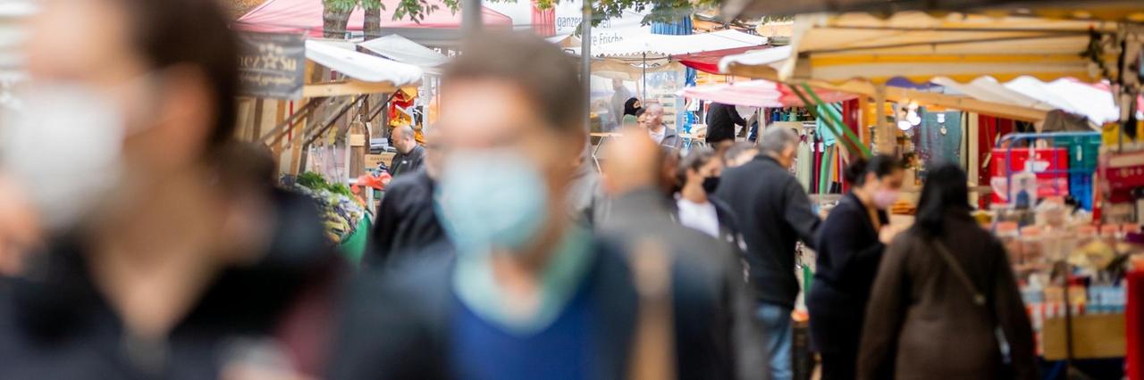 Menschen tragen Mund-Nasen-Bedeckungen und gehen in Berlin-Kreuzberg über den Markt am Maybachufer.