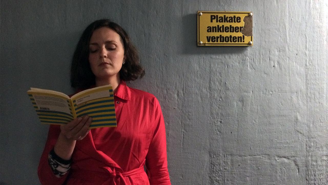 An Bahnhof Eberbach liest eine Frau mit einem roten Mantel aus einem Buch.