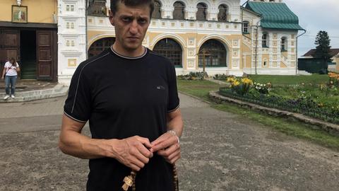 Der russische Ex-Häftling Sanja steht mit einer Holzkette mit Kreuz in der Hand vor einer Kirche in Tutajew