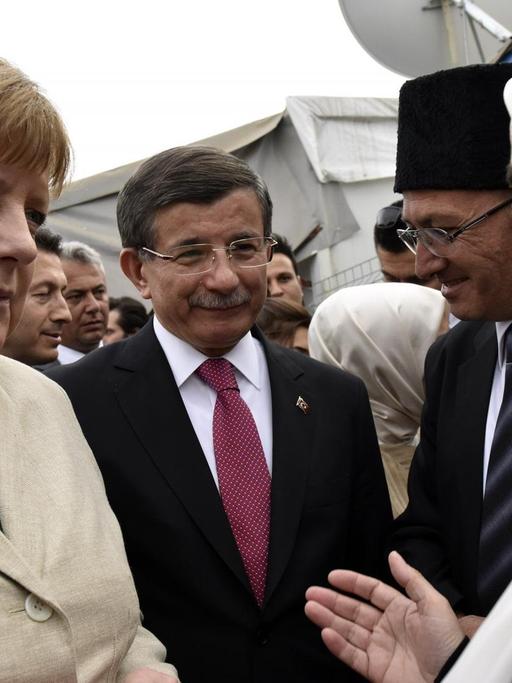Bundeskanzlerin Angela Merkel (l.) unterhält sich gemeinsam mit dem türkischen Ministerpräsidenten Ahmet Davutoglu (M) im Flüchtlingslager Nizip mit Bewohnern des Lagers.