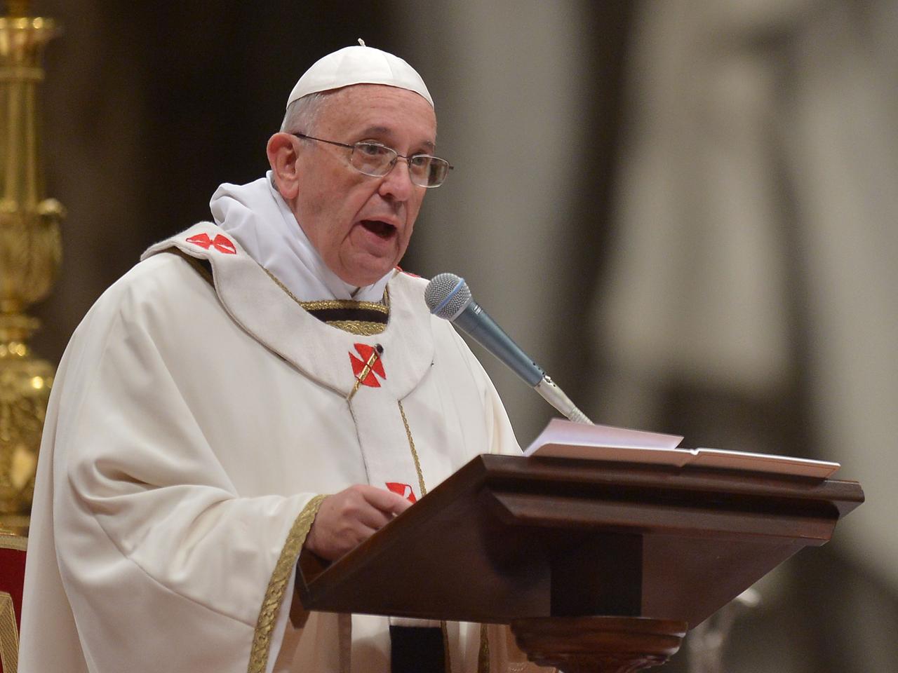 Papst Franziskus spricht hinter einem Rednerpult stehend in ein Mikrofon.