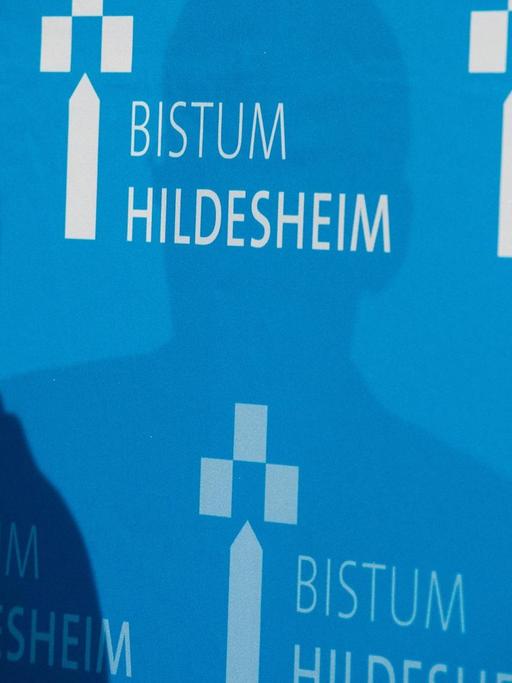 Bei einer Pressekonferenz sind Schatten auf einer Wand mit dem Aufdruck "Bistum Hildesheim".