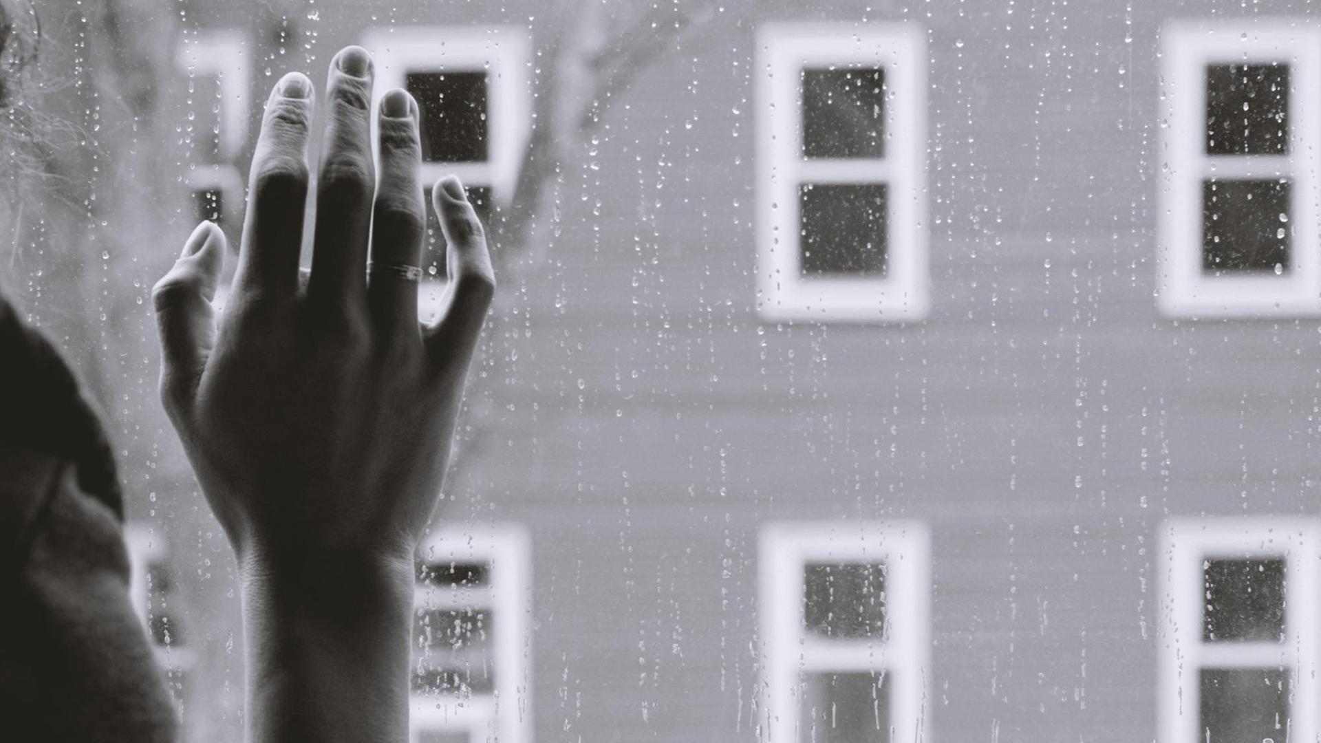 Melancholisches Schwarzweiß-Foto einer Hand, die auf einem Fenster liegt.