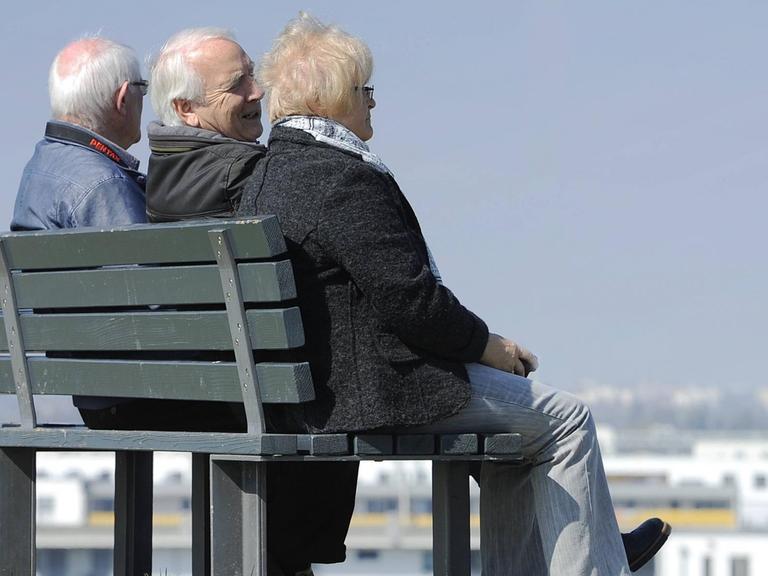Drei Senioren (zwei Männer und eine Frau) sitzen auf einer Bank.