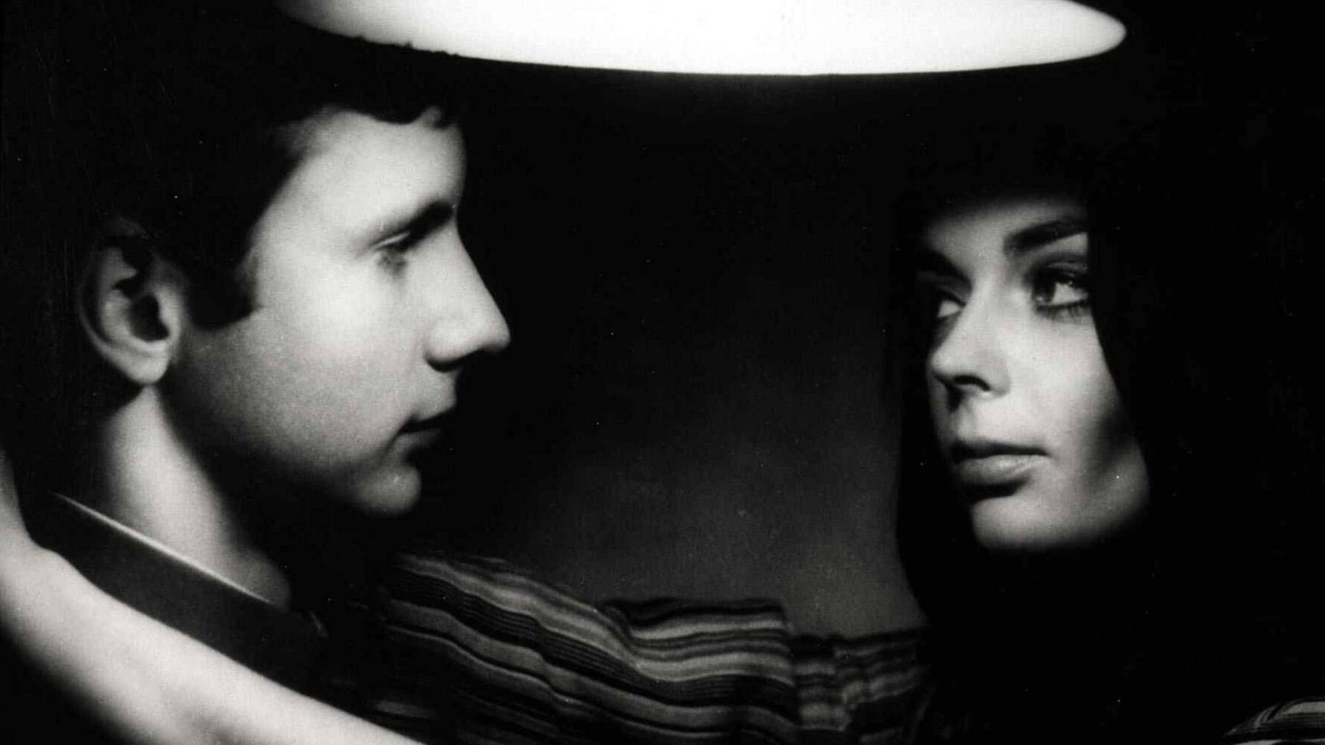 Filmszene, schwarz-weiß: Ein junger Mann und eine junge Frau stehen sich nah gegenüber und schauen sich an, ihre Arme um seinen Hals.
