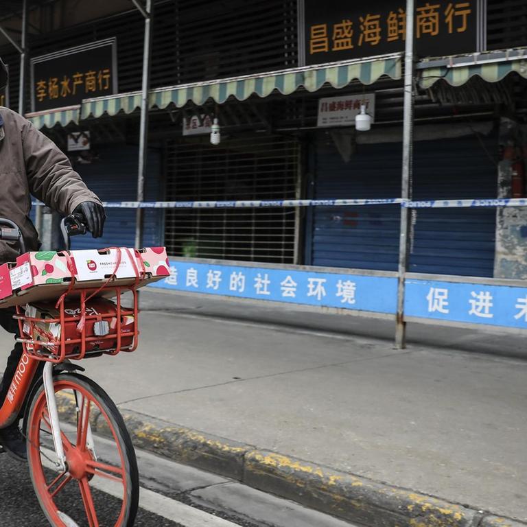 Ein Mann trägt eine Maske, während er auf einem Mobike an dem geschlossenen Huanan-Großmarkt für Meeresfrüchte vorbeifährt, der mit Fällen von Coronavirus in Verbindung gebracht wurde