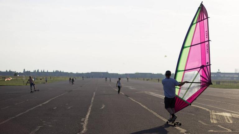  Ein Besucher fährt auf dem als Tempelhofer Freiheit bezeichneten ehemaligen Flughafen Tempelhof in Berlin mit einem Windsegel Longboard